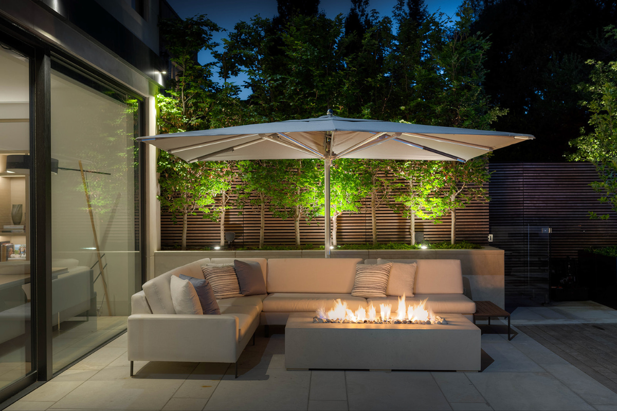 Lit Dekko firepit outdoors at night, creating a cozy ambiance for entertainment, complemented by a stylish sectional under a spacious umbrella