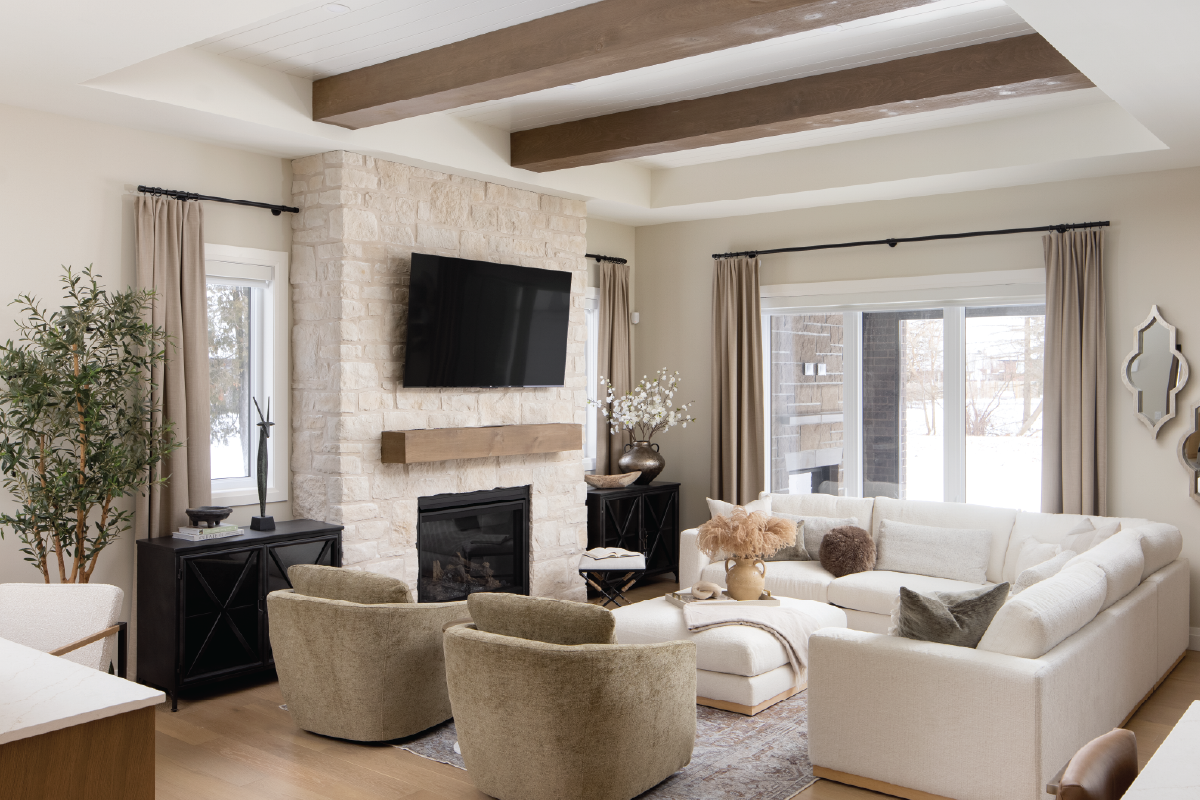 Forest Trail model home completed living room featuring a stone fireplace, wood beams, neutral sectional sofa, and warm, layered textures.