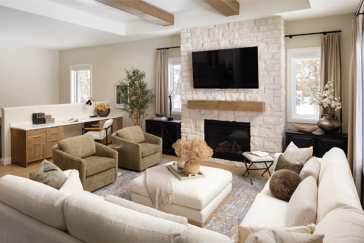 Forest Trail model home living room with stone fireplace, wood beam ceilings, cozy neutral furniture, and built-in desk area.