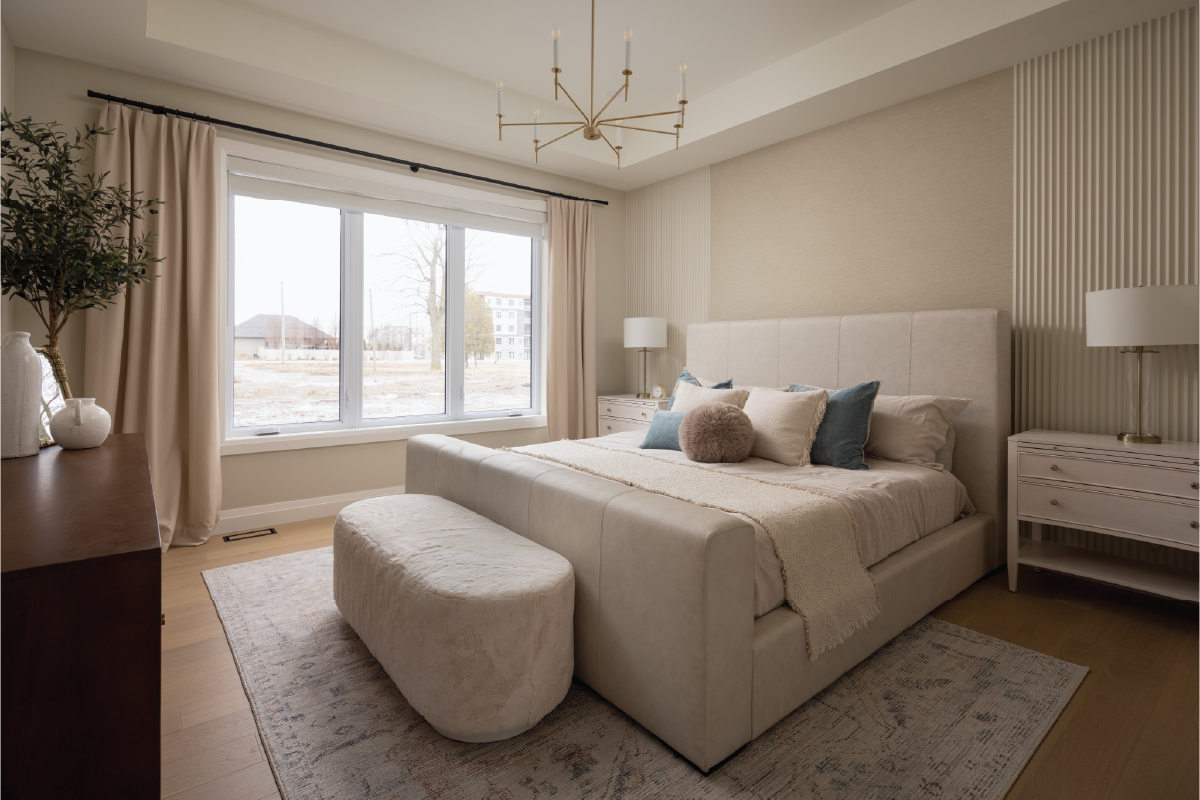 Forest Trail master bedroom featuring a modern upholstered bed, soft neutral palette, gold chandelier, and natural light from large windows.