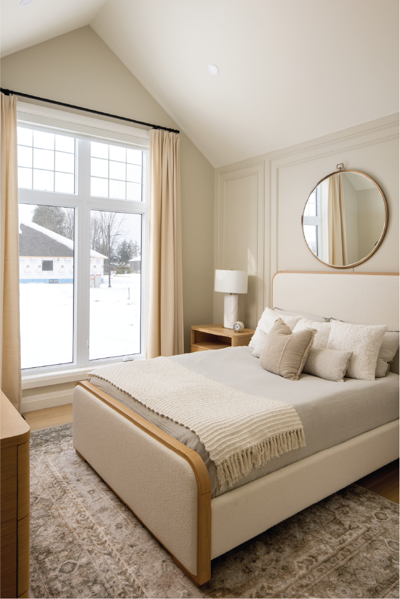 Serene bedroom in Forest Trail model home featuring soft neutral textiles, a wood-framed upholstered bed, and floor-to-ceiling window with natural light.