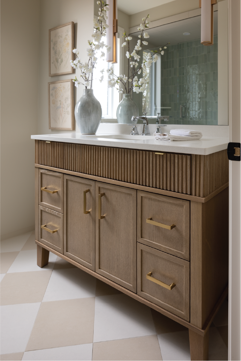 Natural wood vanity with gold hardware, textured detailing, and soft neutral styling in Forest Trail model home bathroom.