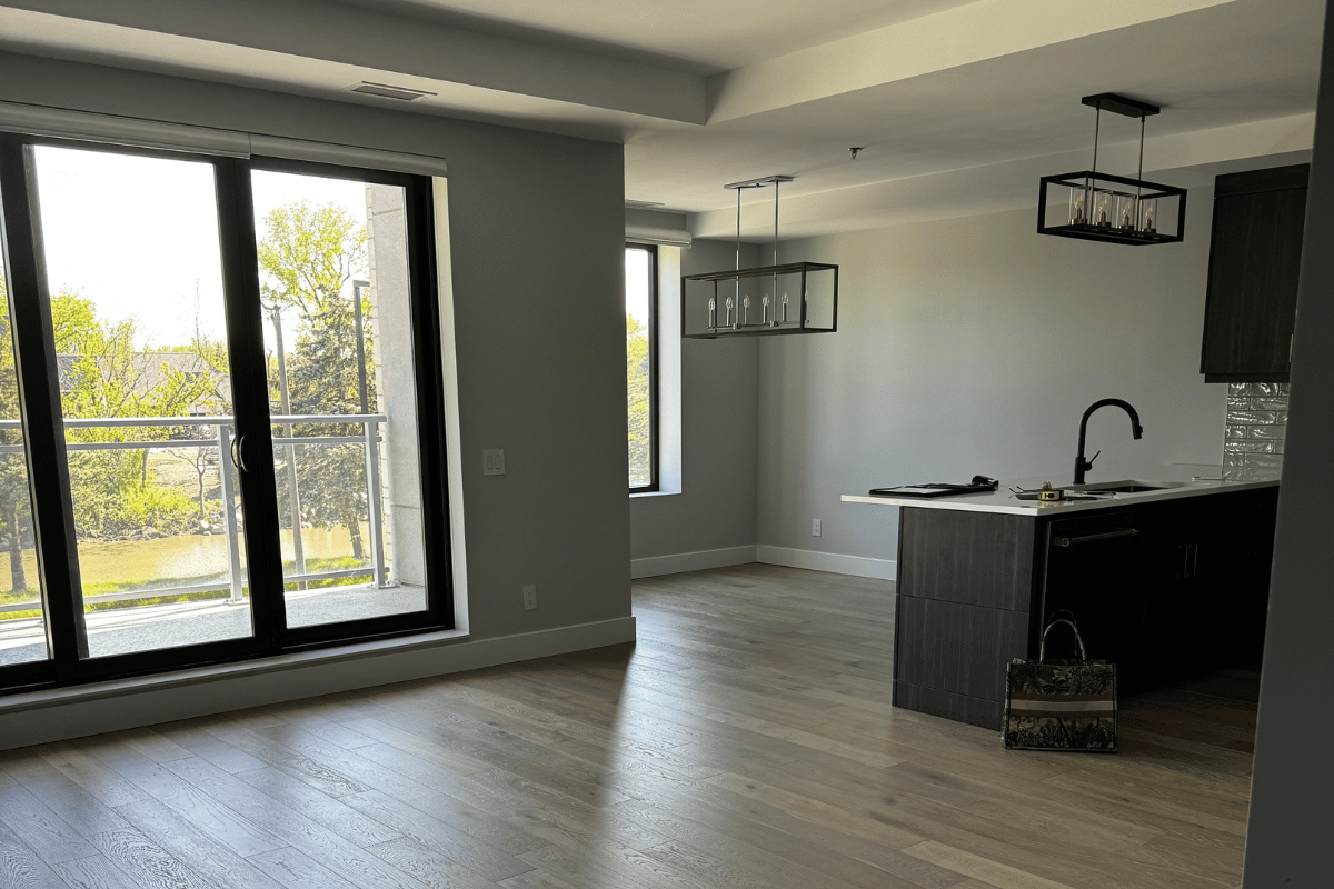 Before photo of a condo interior with an open layout, dark kitchen cabinets, and large windows letting in natural light.