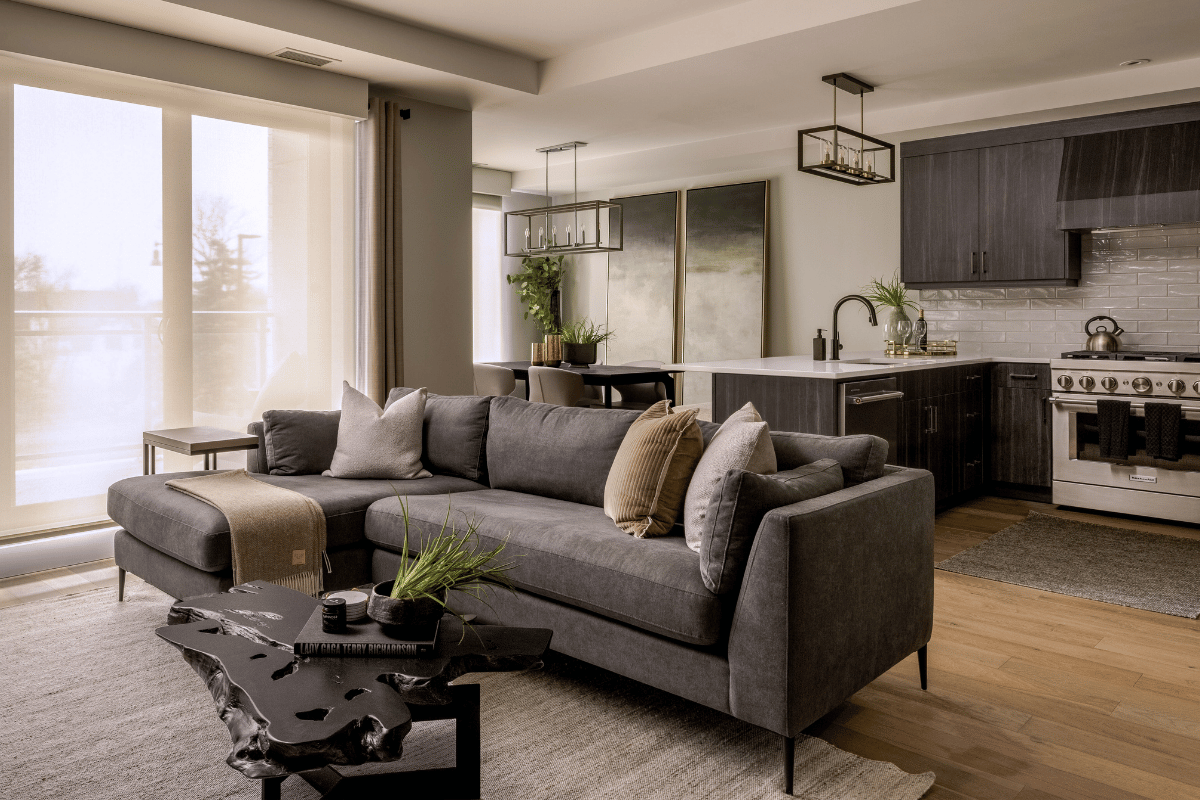 After photo of a beautifully styled condo with a dark grey sectional, abstract art, kitchen island, and integrated dining area.