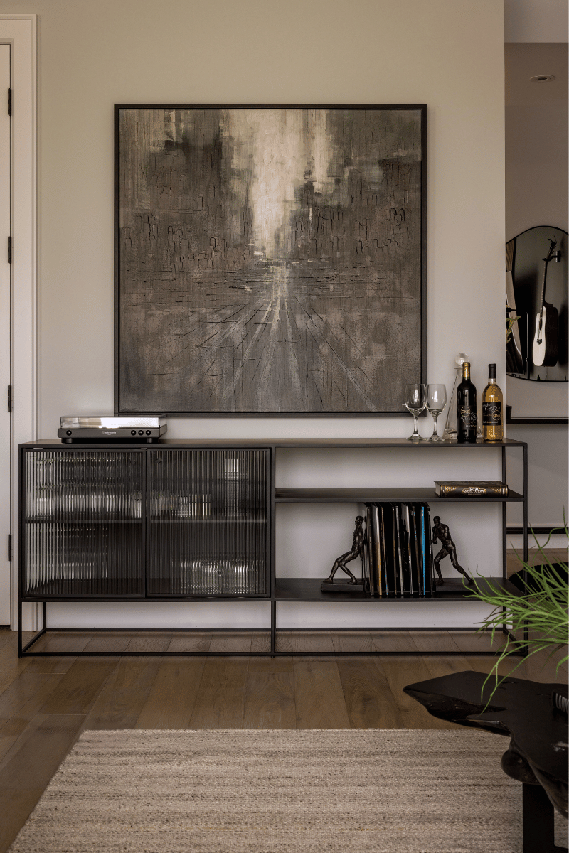 Modern black console with fluted glass doors and styled shelving, featuring urban artwork, glassware, and curated books.