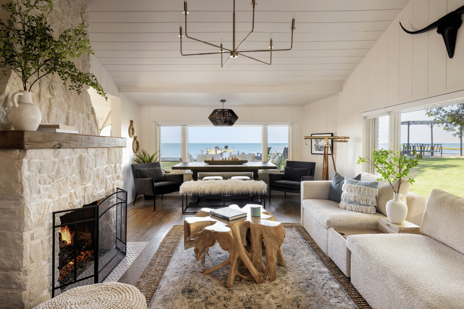 Lakehouse living room with panoramic lake view, featuring a stone fireplace, modern furnishings, and rustic coastal decor.