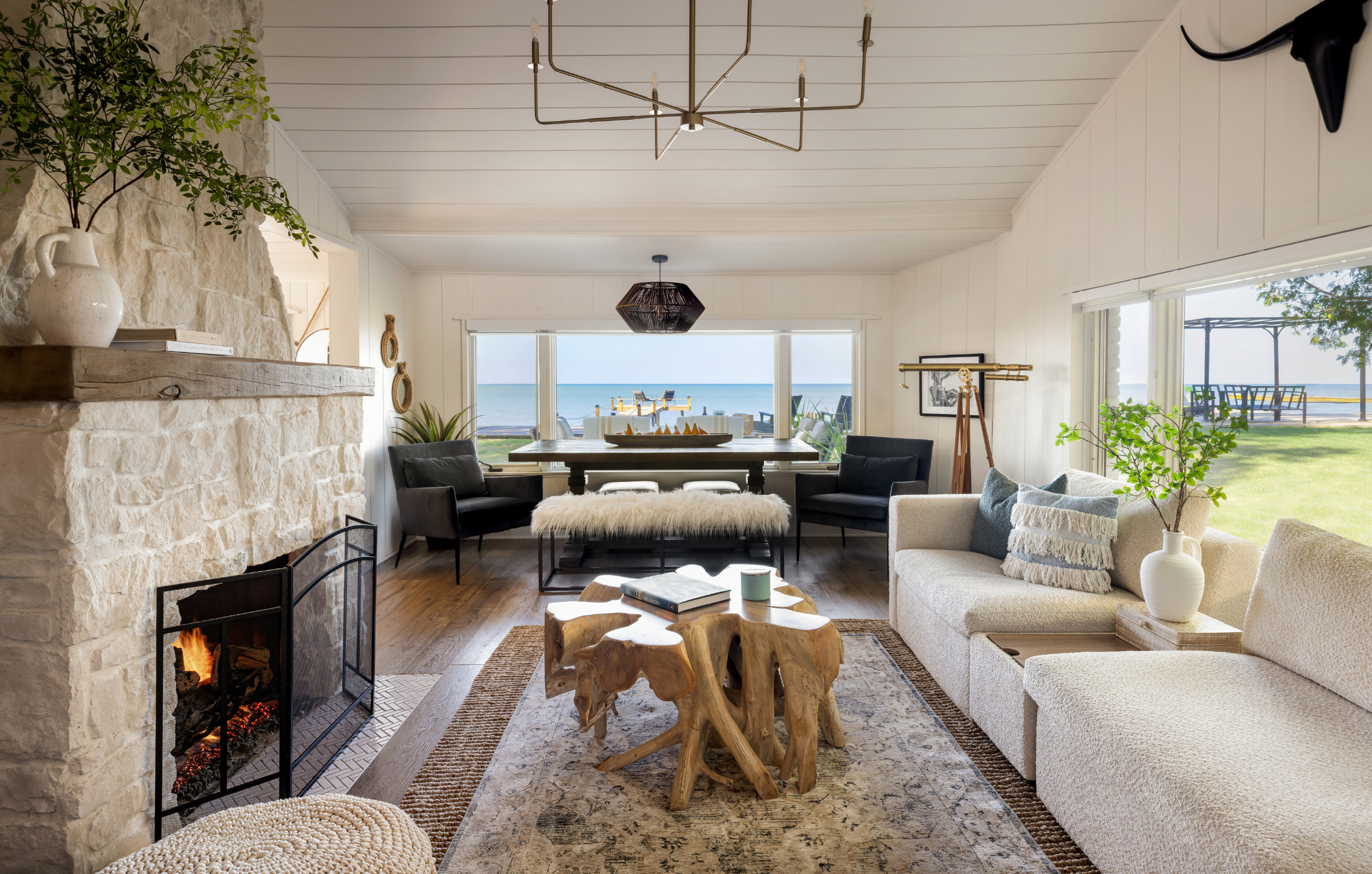 Lakehouse living room with stone fireplace, rustic wood coffee table, and panoramic lake views.