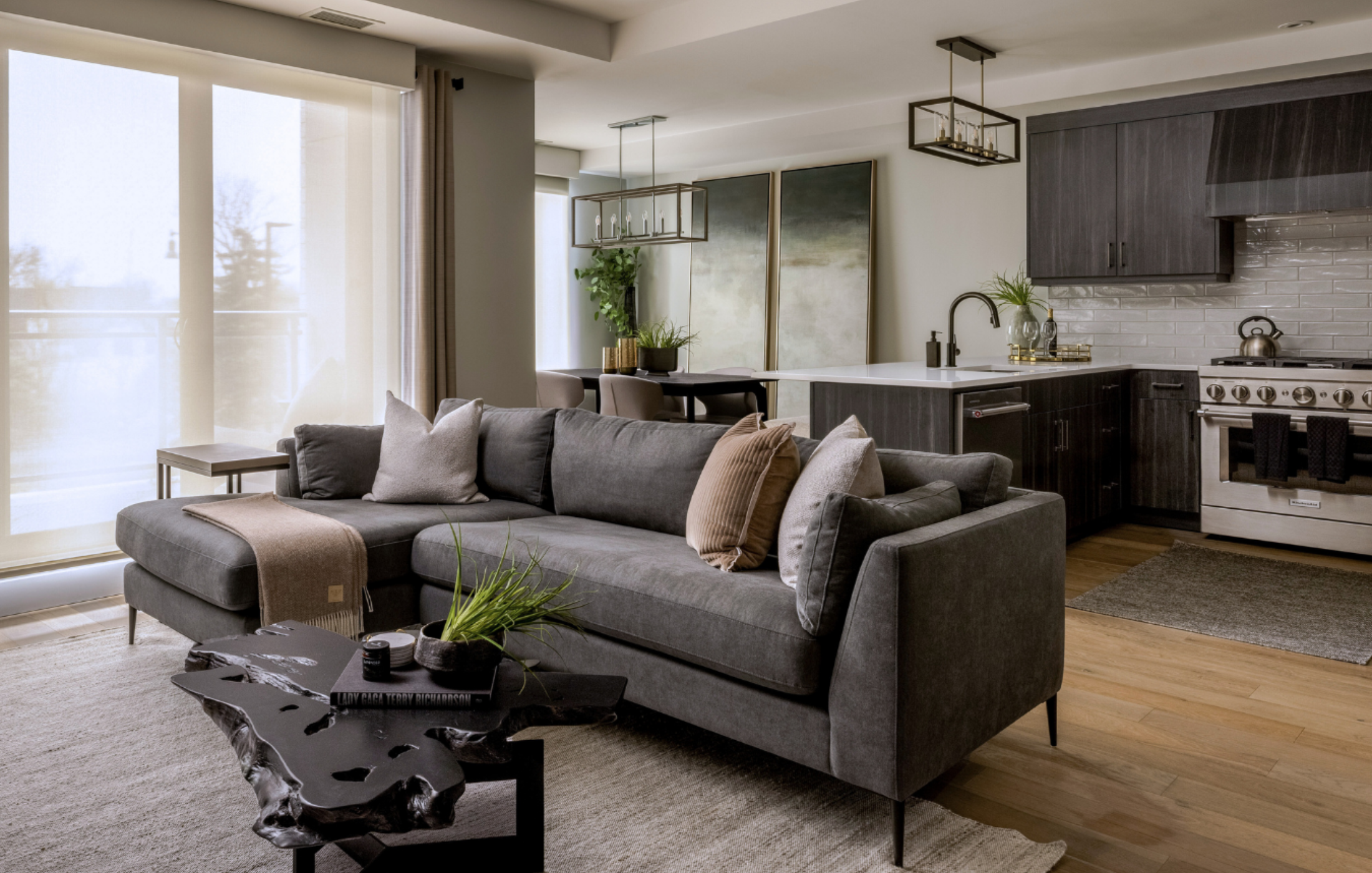 Open-concept condo living space with grey sectional, modern kitchen, and abstract art.