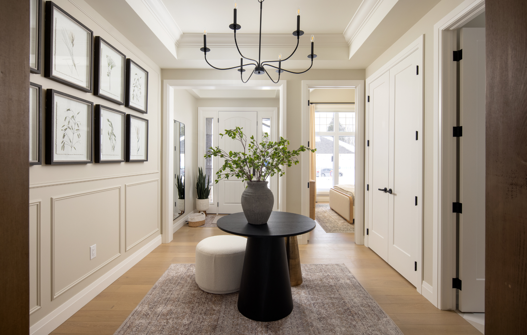 Modern entryway with black chandelier, botanical wall art, and round accent table with greenery.